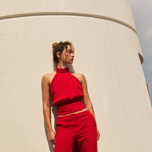 May include: A vibrant red two-piece set consisting of a sleeveless halter-neck top with a gathered high neckline and a wide waistband, paired with matching long, straight-leg trousers. The ensemble features a solid, bold red colour throughout.