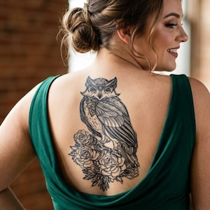 May include: A sleeveless emerald green dress with a deep scoop back, featuring a large black ink tattoo on the upper back depicting a detailed owl perched atop a cluster of blooming roses with intricate line work and shading throughout the design.