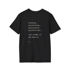 May include: A black short-sleeved t-shirt featuring white text that reads: thinking... overthinking... paralysed by possibilities... just prompt it and move on. Below the text is a small green command line prompt symbol consisting of a greater than sign and underscore.