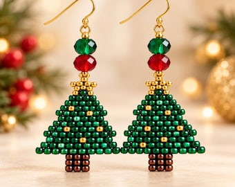 Peut inclure: Une paire de boucles d'oreilles pendantes en forme de sapin de Noël perlées en vert et or, surmontées d'une pile de perles en cristal rouge et vert. Les boucles sont suspendues à des crochets dorés et présentent un tronc en perles marron.