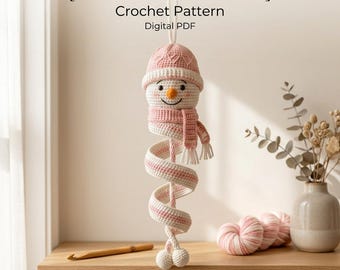 Peut inclure: Une décoration de bonhomme de neige en crochet en spirale avec un bonnet et une écharpe roses, portant le texte [SPIRAL SNOWMAN] Crochet Pattern Digital PDF. Le bonhomme a un visage blanc, un nez orange et un long corps en spirale.