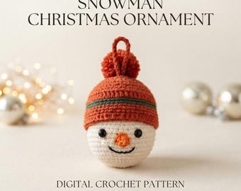 Peut inclure: Une décoration de Noël bonhomme de neige au crochet avec une tête sphérique blanche, un petit nez carotte orange, des yeux en perles noires et un sourire brodé. Il porte un bonnet orange à rayure verte et pompon. Texte : SNOWMAN CHRISTMAS ORNAMENT DIGITAL CROCHET PATTERN.