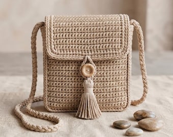 Peut inclure: Un sac bandoulière en crochet beige doté d'un corps rectangulaire avec un rabat, un bouton en bois unique et un pompon assorti. Le sac comprend une bandoulière tressée et est réalisé avec un motif de points dense et uniforme.