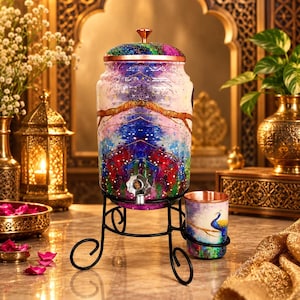 May include: A cylindrical water dispenser with a vibrant, multi-coloured abstract pattern featuring shades of blue, pink, and purple. It has a copper-toned lid, a metal spigot, and rests on a black wire stand. A matching cup with a peacock design is included.