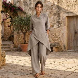 May include: A beige two-piece set consisting of a long-sleeved wrap tunic with an asymmetrical hemline and matching wide-leg trousers. The tunic features a V-neckline and side pockets, while the trousers have a loose, relaxed fit.