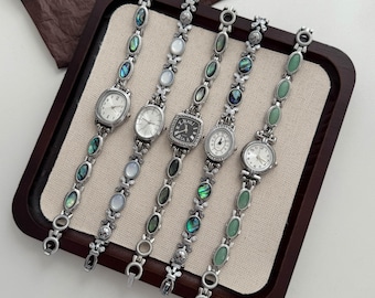 May include: Five silver-toned wristwatches with link bracelets featuring oval inlays of iridescent abalone shell, white mother-of-pearl, and green stone. The watches have varied dial shapes including oval, round, and square with analog displays.