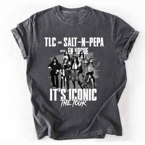 May include: A charcoal grey short-sleeve t-shirt featuring a black and white graphic of the musical groups TLC, Salt-N-Pepa, and En Vogue. The text reads TLC AND SALT-N-PEPA WITH EN VOGUE IT'S ICONIC THE TOUR in a distressed white font style.