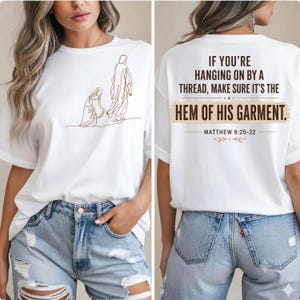 May include: A white t-shirt featuring a brown line art illustration of a person reaching for a garment on the front. The back displays the text: IF YOU'RE HANGING ON BY A THREAD, MAKE SURE IT'S THE HEM OF HIS GARMENT. MATTHEW 9:20-22.