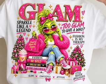 May include: A white t-shirt featuring a graphic of a green character with a pink bow, pink sunglasses, and a pink fur coat. The design includes text like GLAM, SPARKLE LIKE A LEGEND, and FASHION IS MY THERAPY, alongside illustrations of Christmas trees, gifts, and makeup.