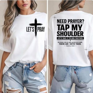 May include: A white t-shirt featuring a black cross graphic on the front with the text LET'S PRAY. The back displays the text NEED PRAYER? TAP MY SHOULDER, LET'S TAKE IT TO GOD TOGETHER, and FOR WHERE TWO OR THREE GATHER IN MY NAME, THERE AM I WITH THEM. MATTHEW 18:20.
