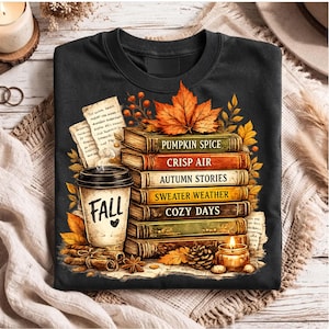 May include: A black crewneck t-shirt featuring a graphic of a stack of books titled Pumpkin Spice, Crisp Air, Autumn Stories, Sweater Weather, and Cozy Days, next to a coffee cup labelled Fall, cinnamon sticks, a candle, and autumn leaves.