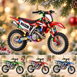 May include: A red dirt bike ornament featuring the name MASON printed on the side panel. The motorcycle is wrapped in colorful string lights and hangs from a gold cord. The design includes black knobby tires, a silver exhaust, and white accents.