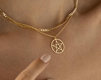 May include: A gold-toned layered necklace featuring a delicate curb chain and a secondary chain with a circular pendant. The pendant displays an open-work pentagram design. The necklace rests against the neck, showcasing a polished metallic finish.