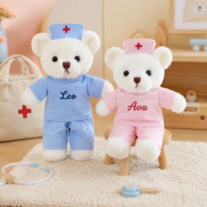 May include: Two white plush teddy bears dressed as medical professionals. One bear wears a blue scrub top with the name Leo and a blue cap with a red cross. The other bear wears a pink scrub top with the name Ava and a pink cap with a red cross.