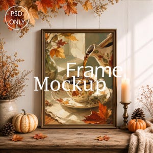 May include: A rectangular gold-toned frame containing an illustration of coffee being poured into a teacup, surrounded by autumn leaves, a pumpkin, a candle in a brass holder, and a pinecone on a wooden surface with the text PSD ONLY Frame Mockup.