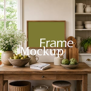 May include: A horizontal rectangular wooden frame with a solid olive green interior, positioned on a rustic wooden table. The scene includes a bowl of pears, a white pitcher, a stack of folded linens, and a bowl of artichokes on the table.