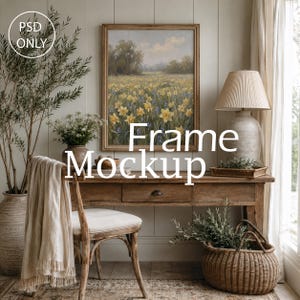 Op de afbeelding: Een rechthoekige houten lijst-mockup met een schilderij van een veld met gele narcissen onder een bewolkte lucht. De lijst hangt centraal aan een muur boven een houten bureau met een lamp, een stoel met een doek en een rieten mand met groen.