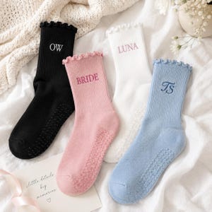May include: Four ribbed crew socks with ruffled cuffs and non-slip grips on the soles. The black sock features the embroidered text OW, the pink sock says BRIDE, the white sock says LUNA, and the light blue sock displays the monogram Ts.