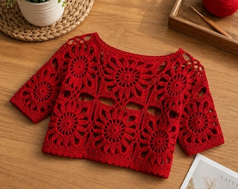 May include: A vibrant red crochet top constructed from multiple square motifs featuring a central floral pattern. The garment has short sleeves, a wide neckline, and an openwork design throughout, showcasing the intricate yarn stitching.