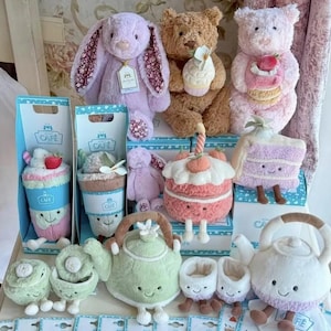 Peut inclure: Une collection de peluches comprenant un lapin lavande, un ours brun tenant un cupcake, un ours rose avec une fraise, une part de gâteau en peluche, une théière verte, une théière blanche et divers petits objets en peluche souriants.