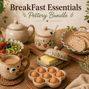 May include: A 7-in-1 pottery breakfast bundle featuring a speckled teapot, a lidded sugar bowl with strawberry motifs, a butter dish with a lid, a flower-shaped egg holder with six eggs, a bear-shaped mug, and two scalloped serving bowls.
