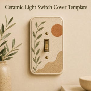 May include: A rectangular ceramic light switch cover with a speckled beige finish. The design features a green leafy branch on the left, a textured orange circle in the upper right, and a tan wavy landscape at the bottom. It includes a central toggle switch.