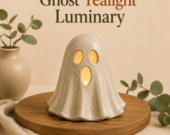 May include: A ceramic ghost tealight luminary with a speckled beige finish. The ghost figure features two oval eye cutouts and a larger oval mouth cutout, allowing warm light to glow from within. The text Ghost Tealight Luminary is visible.