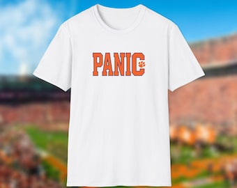 May include: A white short-sleeved t-shirt featuring the word PANIC printed in bold orange block letters across the chest, with a small orange paw print icon positioned to the right of the letter C in a collegiate athletic font style.