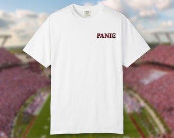 May include: A white short-sleeve crew neck t-shirt featuring the word PANIC printed in dark red capital letters on the upper left chest area, with the letter C replaced by a small dark red and white graphic of a gamecock bird logo.