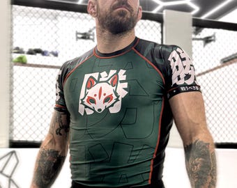 May include: A dark green short-sleeve compression shirt featuring a white and red fox graphic on the chest, black side panels, and white Japanese characters on the sleeves. The shirt is paired with black athletic shorts with white text details.