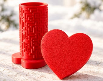 Può includere: Un contenitore cilindrico rosso brillante caratterizzato da un intricato motivo a labirinto sull'esterno, abbinato a un coperchio separato a forma di cuore di colore rosso pieno. Gli oggetti sono realizzati in materiale testurizzato.