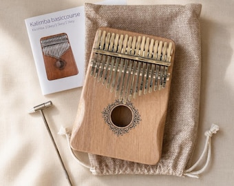 Può includere: Una kalimba in legno marrone chiaro con diciassette lamelle metalliche e un foro di risonanza circolare con un'incisione floreale decorativa. Il set include un piccolo martello accordatore in metallo, una sacca beige e un libretto di istruzioni.
