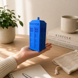 Puede incluir: Un modelo tridimensional rectangular de color azul brillante que representa una cabina de policía. La estructura presenta un techo escalonado, paneles empotrados en los laterales y el texto POLICE PUBLIC CALL BOX en relieve en la parte superior.