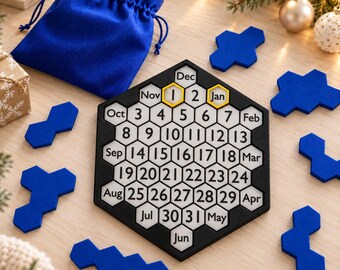 Può includere: Un puzzle calendario perpetuo esagonale con cornice nera e tessere esagonali bianche che mostrano i numeri da 1 a 31 e i mesi da gennaio a dicembre. Include un sacchetto blu con coulisse e diversi pezzi di puzzle blu.