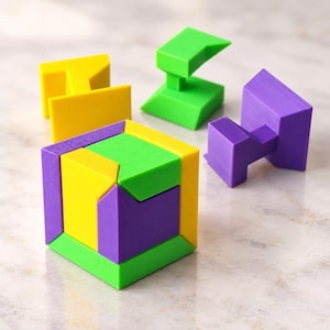 Puede incluir: Un cubo de rompecabezas 3D multicolor ensamblado a partir de piezas geométricas entrelazadas en amarillo brillante, verde lima y morado. Tres componentes de rompecabezas individuales adicionales en los mismos colores se sitúan cerca.