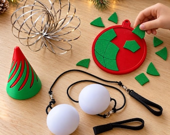 Può includere: Un giocattolo a molla in metallo argentato, un oggetto conico rosso e verde, un puzzle circolare rosso con pezzi in feltro verde e due sfere bianche attaccate a cordini neri con passanti per le dita per oscillare.