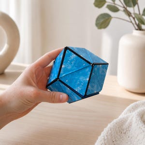 May include: A geometric puzzle toy featuring a blue and white marbled pattern on its triangular faces. The object has a black frame structure that connects the multiple triangular panels, allowing the shape to be manipulated and folded into various forms.