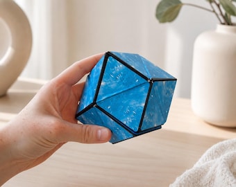 Può includere: Un rompicapo geometrico con un motivo marmorizzato blu e bianco sulle facce triangolari. L'oggetto presenta una struttura a telaio nera che collega i molteplici pannelli triangolari, consentendo di manipolare e piegare la forma in vari modi.