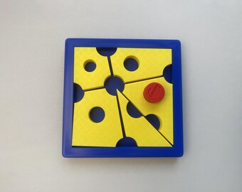 Può includere: Una cornice quadrata blu contenente quattro pezzi di puzzle gialli con ritagli circolari. I pezzi sono disposti in modo da formare un'apertura centrale. Un piccolo gettone circolare rosso con una nota musicale è posto su un pezzo.