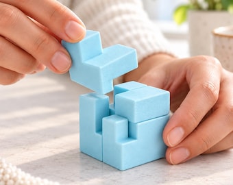 Può includere: Un cubo puzzle in legno azzurro composto da blocchi geometrici a incastro. Un pezzo a forma di L viene inserito nella parte superiore della struttura parzialmente assemblata, caratterizzata da una finitura opaca liscia e un colore pastello uniforme.