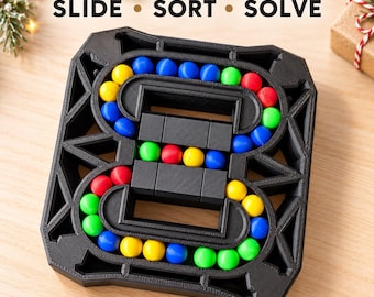 Può includere: Un puzzle game in plastica nera con il testo SLIDE SORT SOLVE. Il tabellone presenta un percorso a forma di otto contenente piccole sfere colorate rosse, blu, gialle e verdi, con un meccanismo centrale scorrevole composto da blocchi neri.