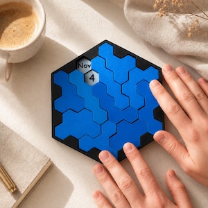 Könnte beinhalten: Ein sechseckiger Puzzle-Kalender mit schwarzem Rahmen und ineinandergreifenden blauen Teilen. Ein Teil ist entfernt, um den Text Nov 4 zu enthüllen. Das Puzzle ist so gestaltet, dass es zur Anzeige des aktuellen Datums neu angeordnet werden kann.