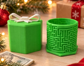 Può includere: Una scatola regalo esagonale verde con un coperchio a fiocco bianco e un contenitore cilindrico verde separato caratterizzato da un intricato motivo a labirinto sulla superficie esterna. Gli oggetti sono realizzati in materiale solido opaco.