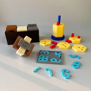 May include: A set of educational math toys including a black storage box with brown, cream, and gray blocks labeled 1016 and 1024, a yellow hexagonal tower with blue and red pegs, additional yellow hexagonal pieces, and blue number-shaped tiles.