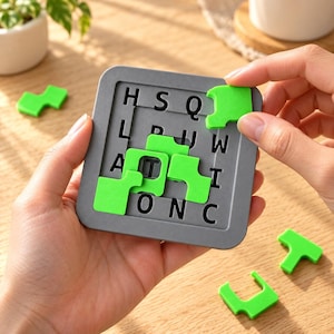 Könnte beinhalten: Ein quadratisches graues Puzzlebrett mit einem Gitter aus schwarzen Buchstaben, darunter H, S, Q, L, P, W, A, T, I, O, N und C. Mehrere hellgrüne, unregelmäßig geformte Puzzleteile liegen auf dem Brett, wobei ein Teil von einer Hand gehalten wird.