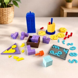 May include: A collection of plastic building blocks and puzzle pieces including a blue police box, yellow hexagonal discs, purple geometric shapes, a brown square container, a gray tray with number cutouts, and a light blue cube puzzle.