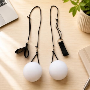 Puede incluir: Dos bolas de poi esféricas de color blanco unidas a cordones negros ajustables. Cada cordón cuenta con un eslabón giratorio de metal, una anilla pequeña y un lazo para el dedo o asa de tela negra. Las esferas blancas mate cuelgan de los cordones.