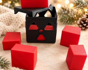 Può includere: Un contenitore quadrato nero con un simbolo di radiazione ritagliato sul lato, accompagnato da un coperchio nero abbinato e cinque solidi blocchi rettangolari rossi. Il contenitore è aperto, con un blocco rosso sopra il coperchio.
