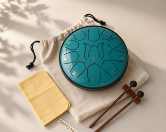 May include: A teal steel tongue drum with a lotus flower design and gold numbered notes, accompanied by a beige drawstring storage bag, a yellow cleaning cloth, and two wooden mallets with black tips, plus a small sticker with the text 56712345671.