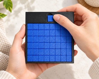 Può includere: Un giocattolo antistress quadrato nero con una griglia di sessantaquattro piccole tessere blu testurizzate. Il dispositivo include un singolo meccanismo a scorrimento blu nella parte superiore centrale per movimenti tattili.